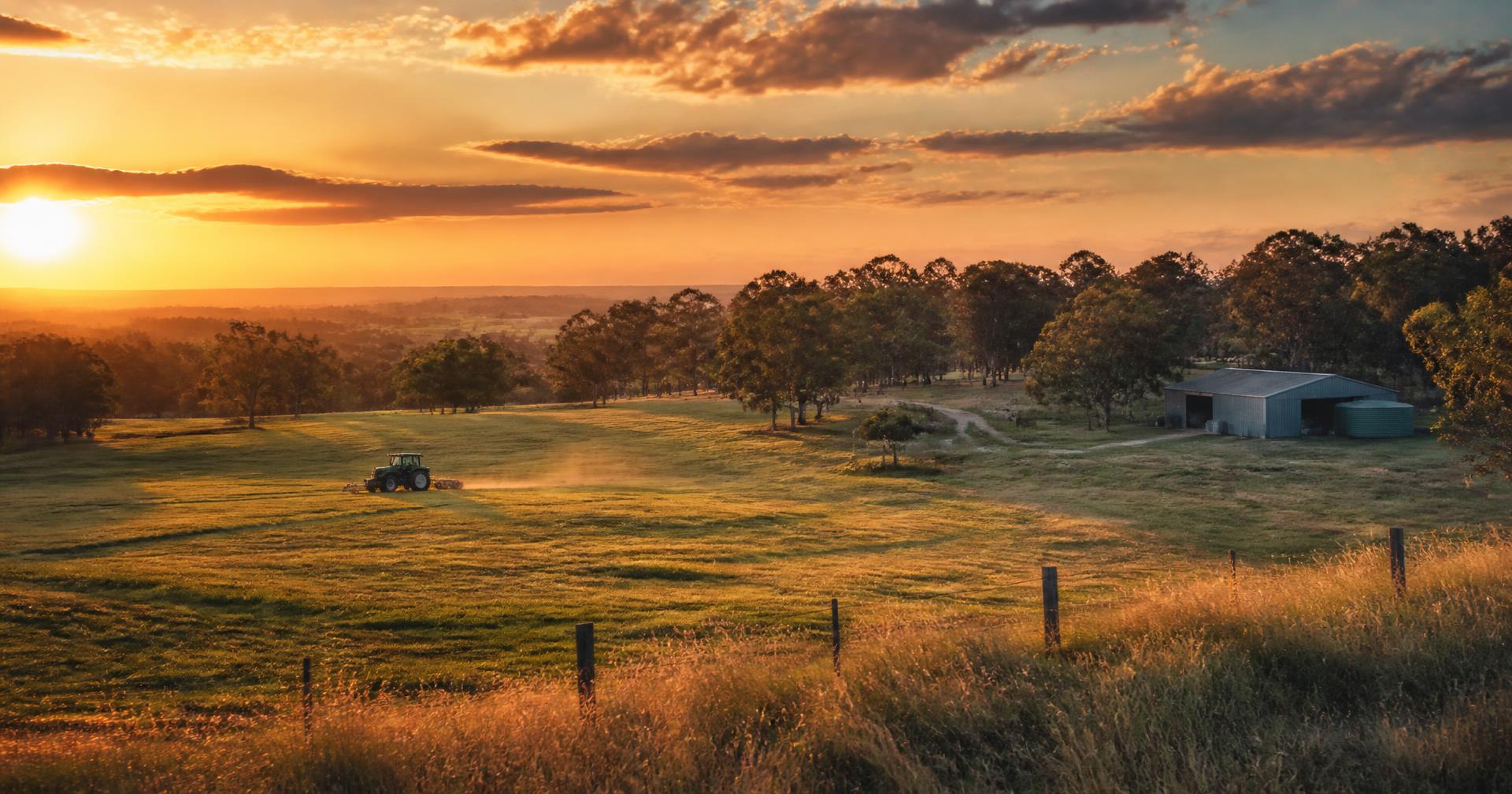 Tractor slashing paddocks on an Australian acreage property at sunset