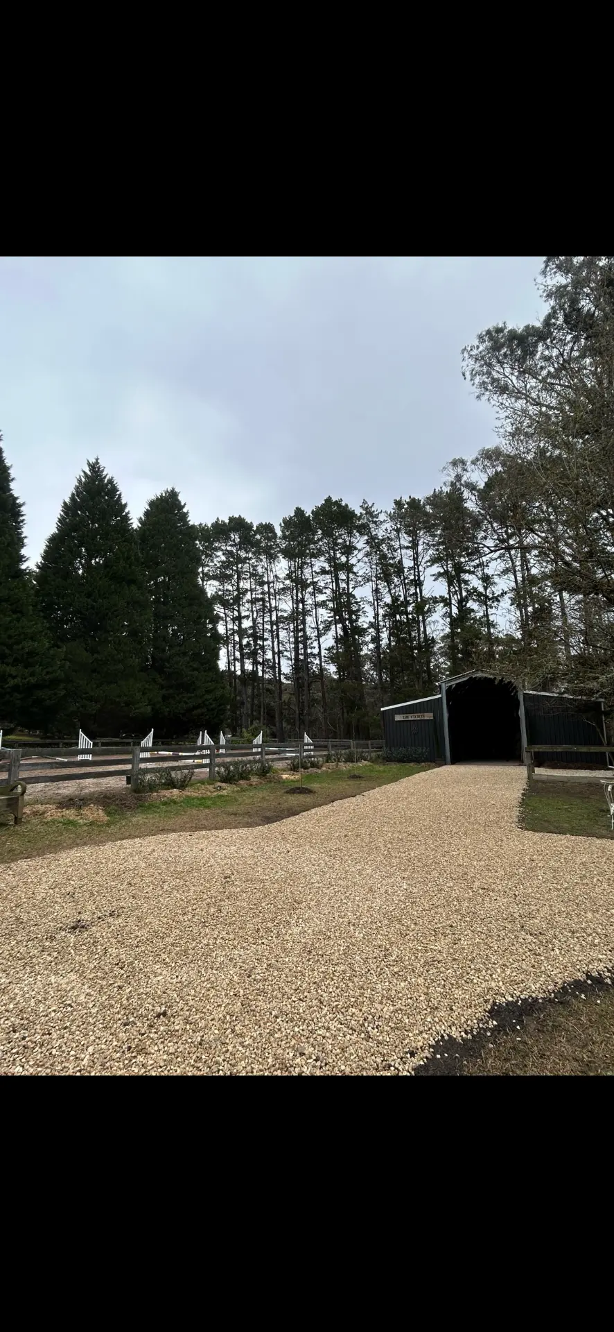New gravel driveway laid up to a green farm shed beside a fenced arena